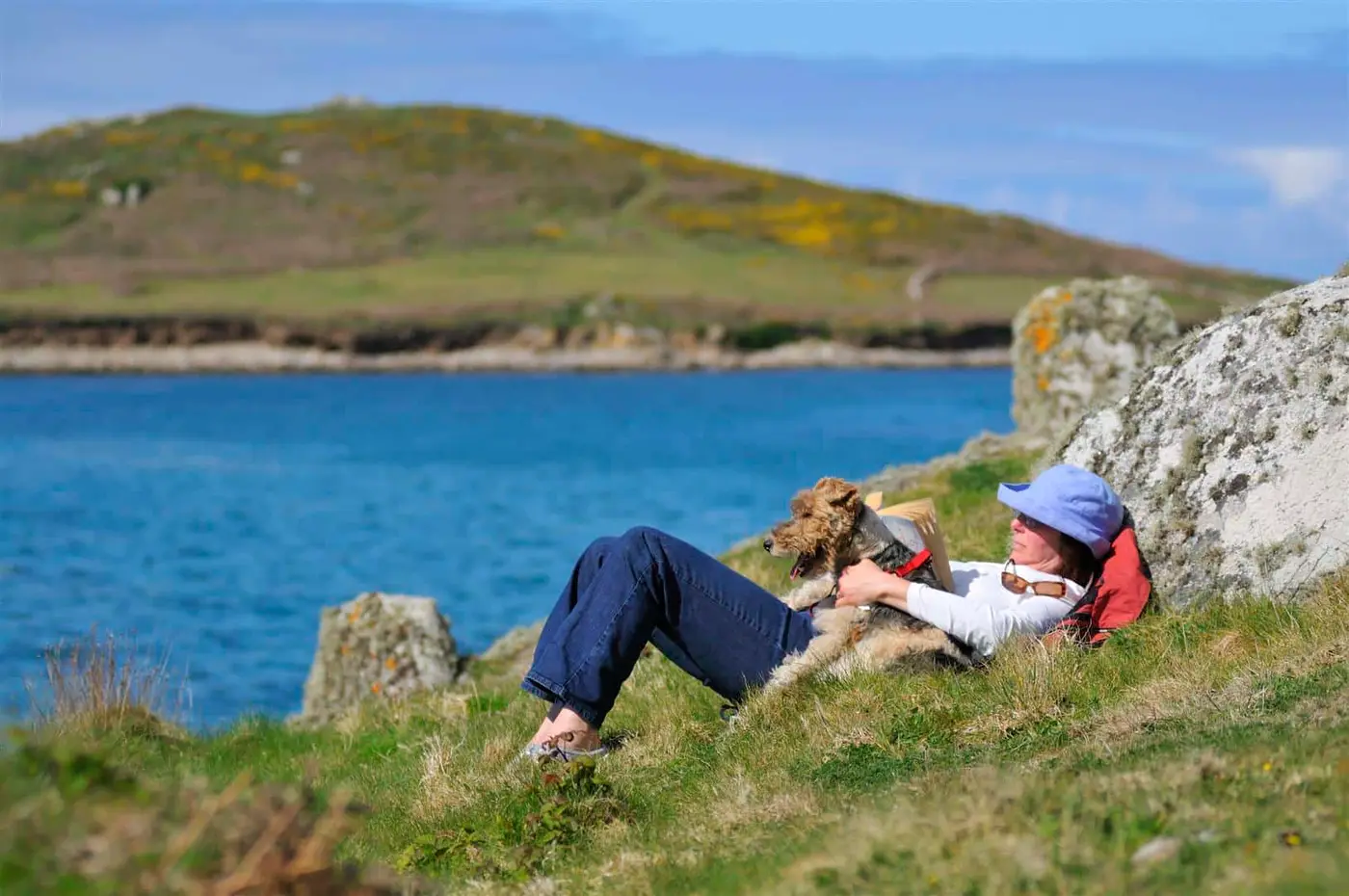 A lady and dog laying in grass beside the sea